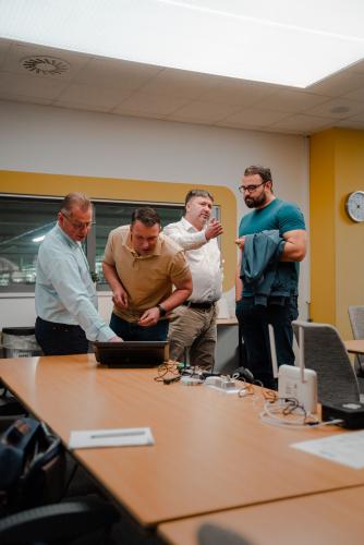 Product Lead MES SoftLi Dušan Keil ukazuje účastníkovi Brunch Meetingu ukázky z MES SoftLi, zatímco další dva hosté spolu živě diskutují